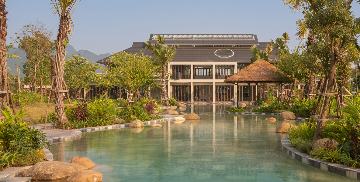 Mandala Retreats Kim Boi resort exterior with a reflecting pool, tropical gardens, and mountains in the background